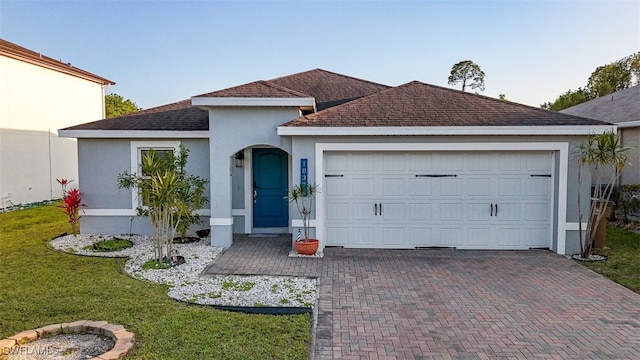 ranch-style house featuring a shingled roof, a front yard, stucco siding, decorative driveway, and an attached garage