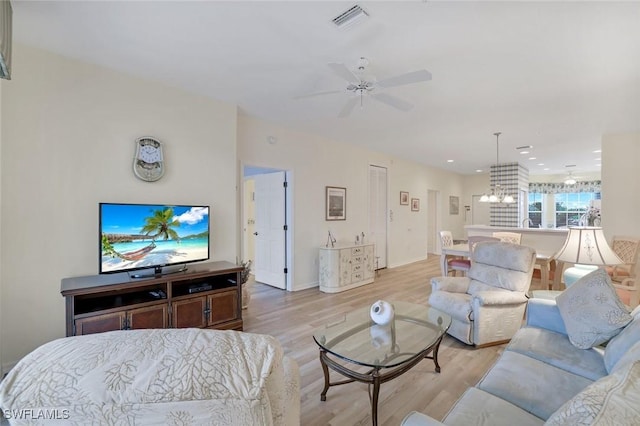 living area with light wood-style floors, visible vents, and ceiling fan with notable chandelier