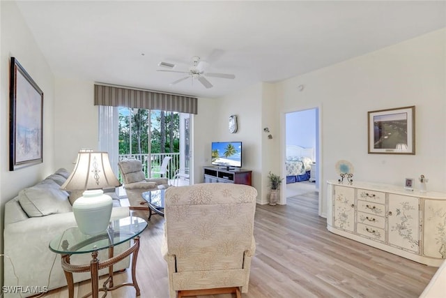 living room featuring light wood-type flooring, ceiling fan, visible vents, and baseboards