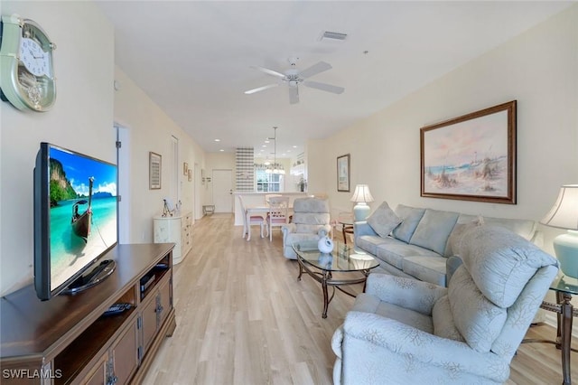 living room featuring visible vents, ceiling fan with notable chandelier, and light wood-style flooring