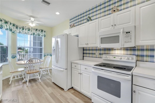 kitchen with light wood finished floors, light countertops, visible vents, white cabinets, and white appliances