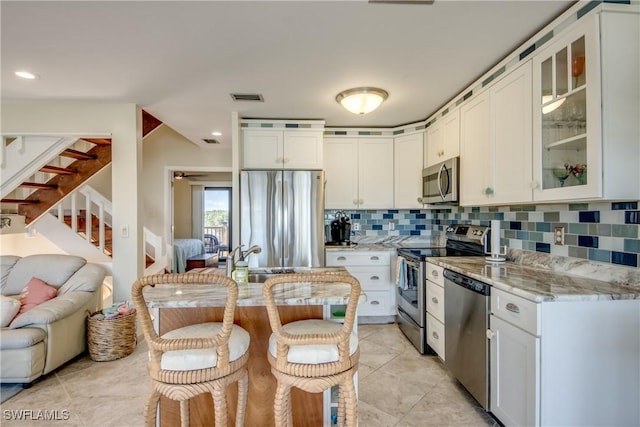 kitchen featuring visible vents, decorative backsplash, light stone counters, open floor plan, and stainless steel appliances