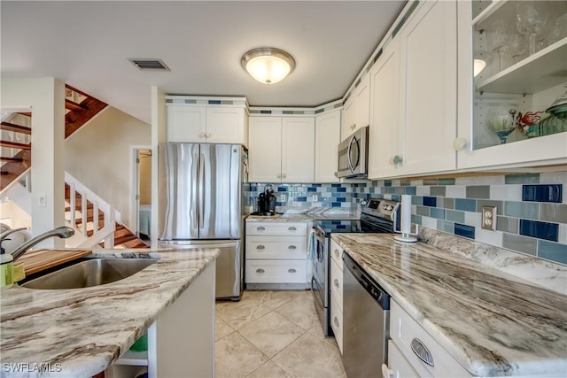 kitchen featuring a sink, white cabinets, appliances with stainless steel finishes, backsplash, and light stone countertops