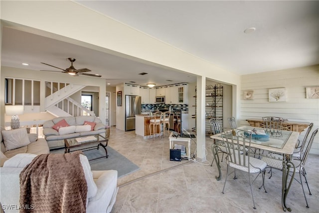 living room with light tile patterned floors, ceiling fan, wood walls, and stairs