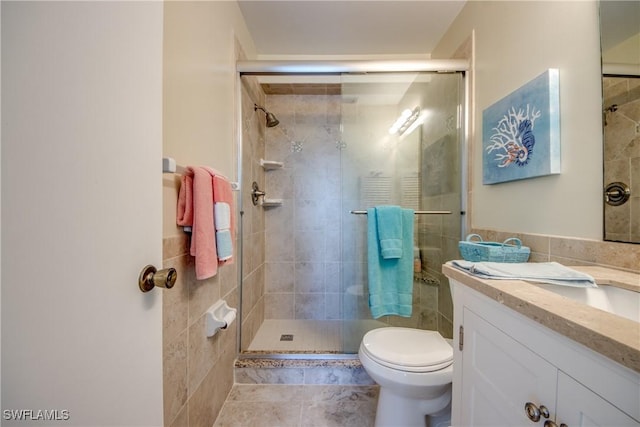 bathroom with a stall shower, toilet, tile patterned floors, vanity, and tile walls