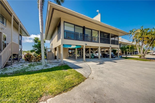 view of front of home with concrete driveway, a sunroom, a carport, a front lawn, and stairs