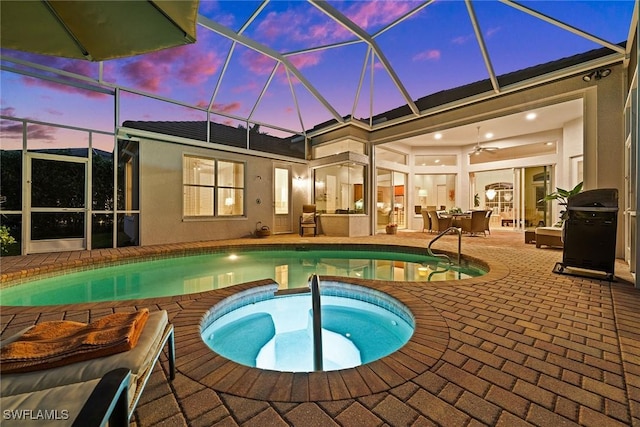 pool at dusk featuring a patio, an outdoor pool, glass enclosure, and an in ground hot tub