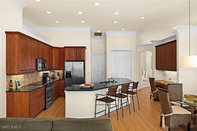 kitchen with arched walkways, a kitchen island with sink, a breakfast bar, appliances with stainless steel finishes, and dark countertops