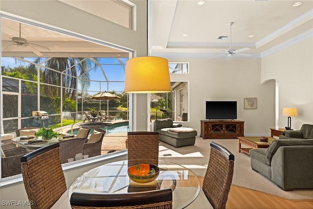 dining space with ceiling fan, ornamental molding, a towering ceiling, and a sunroom