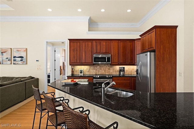 kitchen featuring a sink, ornamental molding, appliances with stainless steel finishes, decorative backsplash, and a kitchen bar