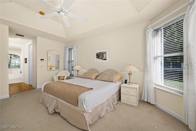 bedroom with a tray ceiling, light carpet, connected bathroom, and baseboards