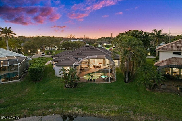 back of house at dusk with glass enclosure, a patio area, an outdoor pool, and a yard