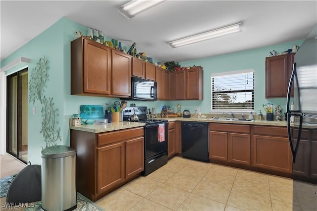 kitchen featuring brown cabinetry, a sink, black appliances, and light tile patterned floors