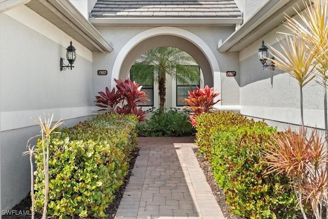 entrance to property featuring roof with shingles, an attached garage, and stucco siding