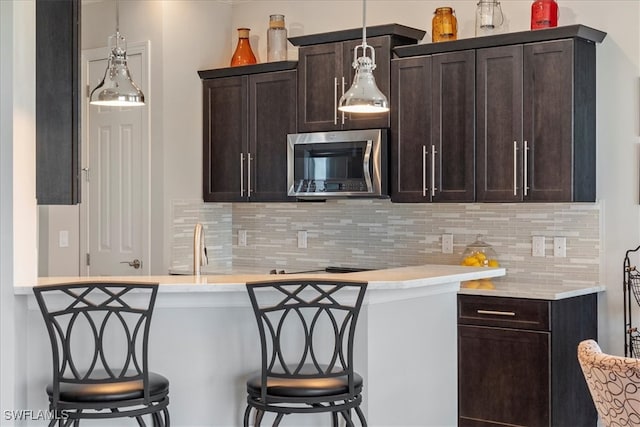 bar featuring stainless steel microwave, hanging light fixtures, and backsplash