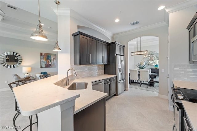 kitchen featuring light stone counters, crown molding, appliances with stainless steel finishes, a sink, and a peninsula