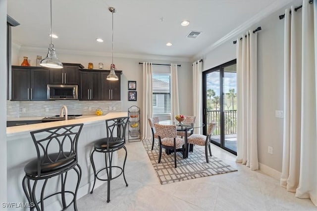 kitchen featuring a breakfast bar area, light countertops, stainless steel microwave, visible vents, and ornamental molding