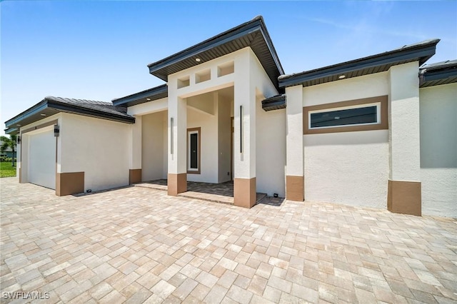 view of exterior entry with a garage, a patio area, and stucco siding