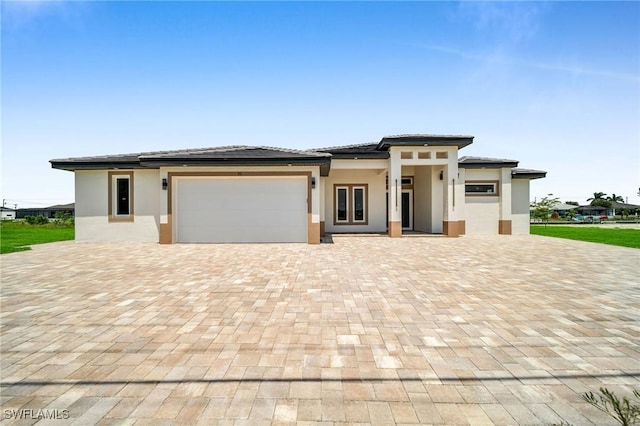 prairie-style home featuring a garage, decorative driveway, and stucco siding