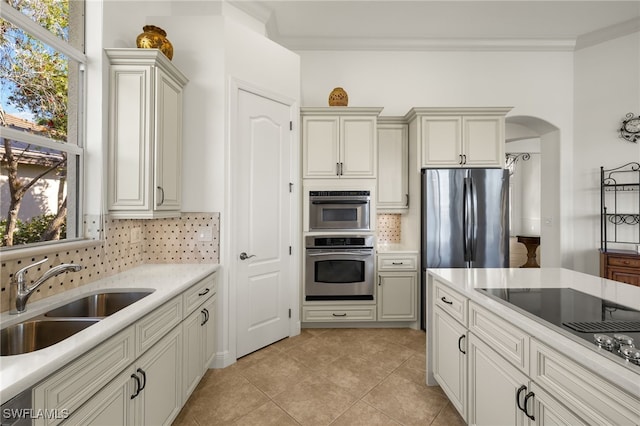 kitchen featuring arched walkways, a sink, light countertops, appliances with stainless steel finishes, and a wealth of natural light