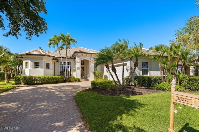 mediterranean / spanish-style house featuring stucco siding, an attached garage, decorative driveway, and a front lawn