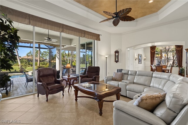 living area featuring light tile patterned floors, a ceiling fan, arched walkways, and ornamental molding