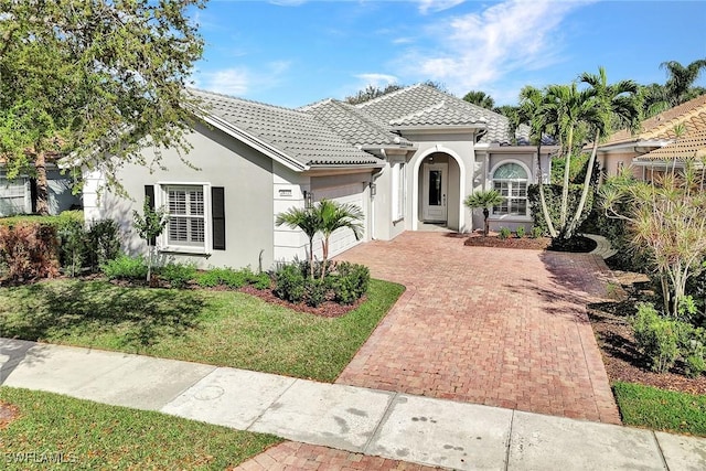 mediterranean / spanish house with an attached garage, a tiled roof, decorative driveway, and stucco siding