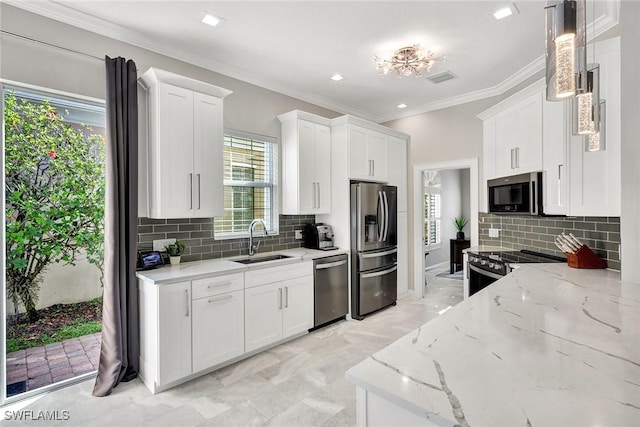 kitchen with a sink, white cabinetry, appliances with stainless steel finishes, light stone countertops, and crown molding