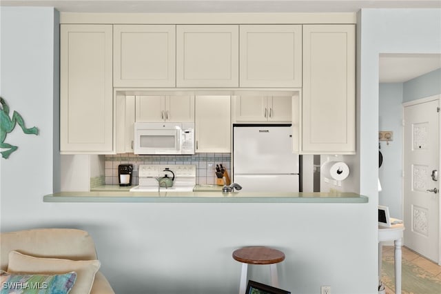 kitchen with white appliances, a breakfast bar area, light countertops, and backsplash