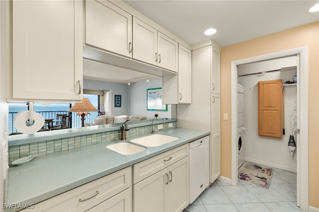 kitchen with light tile patterned floors, a sink, light countertops, stacked washer / drying machine, and dishwasher