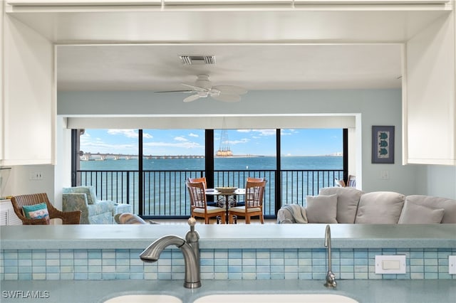 living area featuring a wealth of natural light, a ceiling fan, visible vents, and a water view