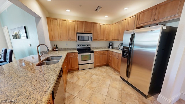 kitchen featuring light stone counters, stainless steel appliances, a peninsula, a sink, and visible vents