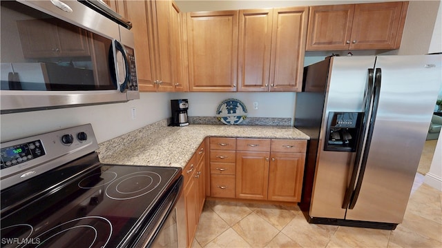 kitchen with appliances with stainless steel finishes, brown cabinetry, and light stone counters