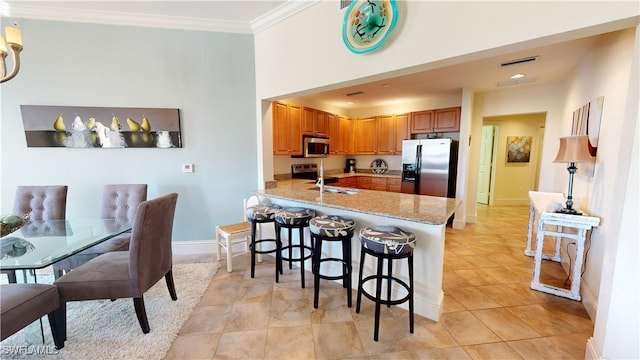 kitchen featuring a breakfast bar, brown cabinets, appliances with stainless steel finishes, ornamental molding, and a peninsula