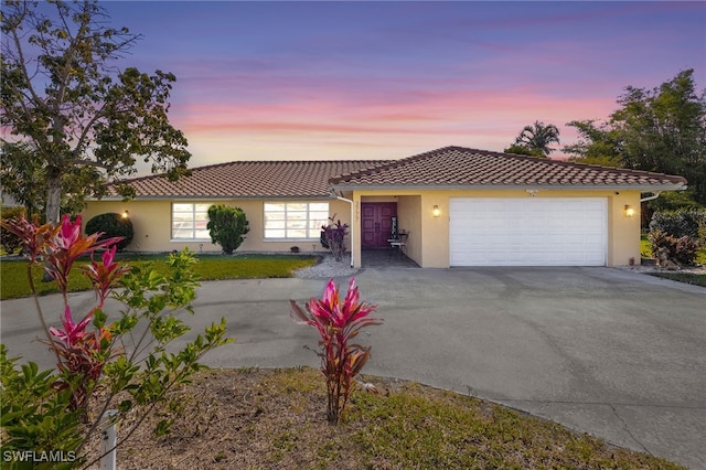 ranch-style home featuring a garage, stucco siding, driveway, and a tiled roof