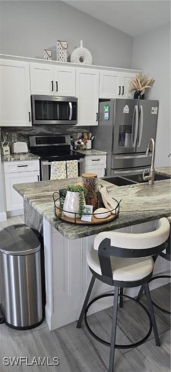 kitchen featuring tasteful backsplash, white cabinets, lofted ceiling, appliances with stainless steel finishes, and a breakfast bar area