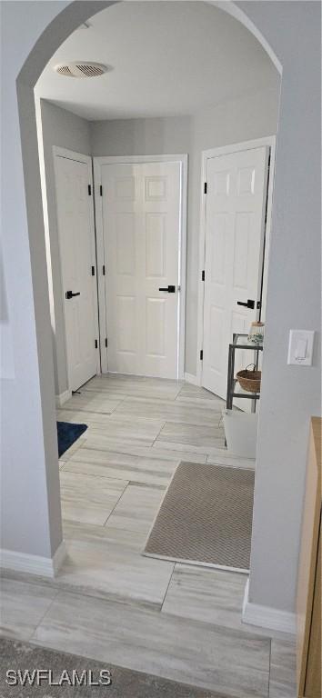 corridor with arched walkways, visible vents, and baseboards