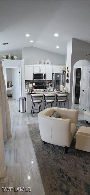 living area with visible vents, arched walkways, washer / clothes dryer, vaulted ceiling, and recessed lighting