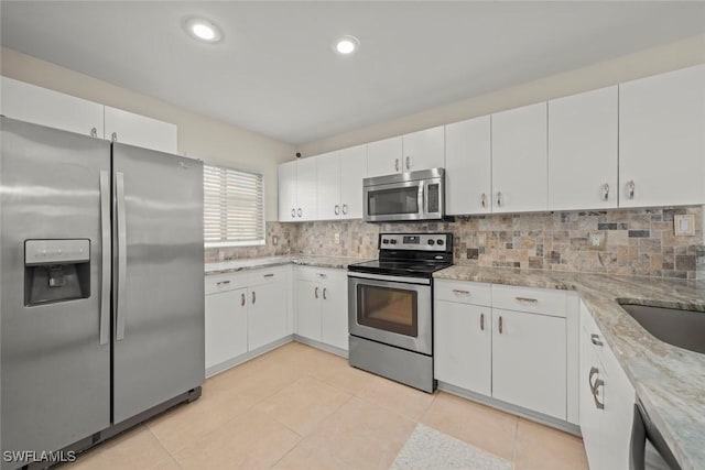 kitchen featuring appliances with stainless steel finishes, light stone countertops, white cabinetry, and tasteful backsplash