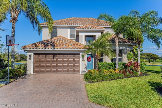 mediterranean / spanish-style house featuring a garage, a front yard, decorative driveway, and stucco siding