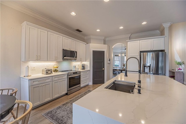 kitchen with arched walkways, backsplash, appliances with stainless steel finishes, a sink, and light wood-type flooring