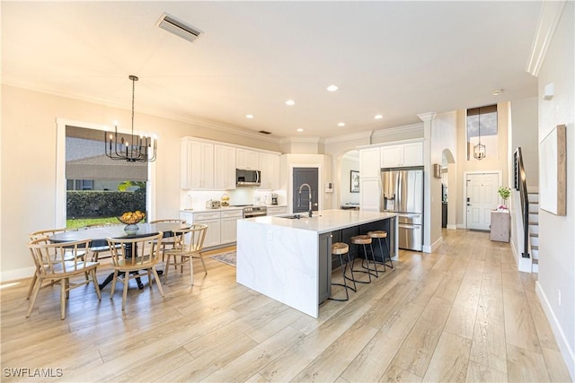 kitchen featuring visible vents, arched walkways, appliances with stainless steel finishes, a breakfast bar area, and a kitchen island with sink