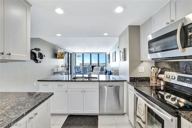 kitchen featuring decorative backsplash, dark stone countertops, appliances with stainless steel finishes, a peninsula, and a sink