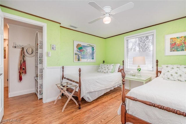 bedroom with light wood-style floors, visible vents, crown molding, and a ceiling fan