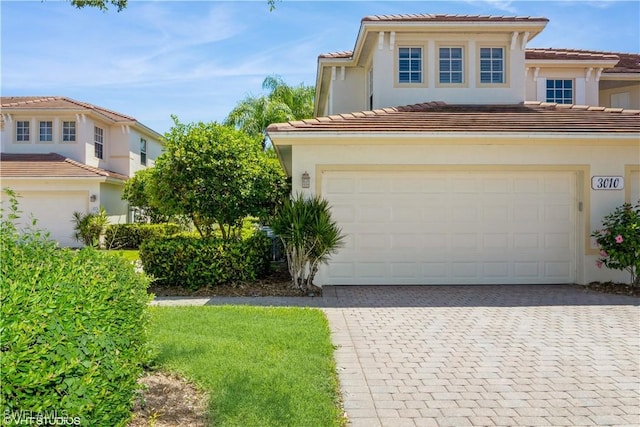 mediterranean / spanish home with decorative driveway, an attached garage, a tile roof, and stucco siding