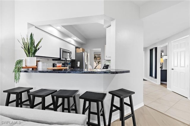 kitchen with white cabinetry, appliances with stainless steel finishes, a kitchen breakfast bar, and backsplash