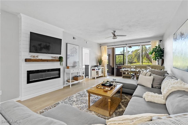 living area with ceiling fan, visible vents, wood finished floors, and a glass covered fireplace