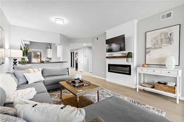 living room with light wood-style floors, visible vents, a fireplace, and baseboards