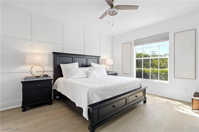 bedroom featuring light wood-style floors, ceiling fan, baseboards, and a decorative wall