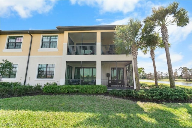 rear view of property with a sunroom, a lawn, a balcony, and stucco siding